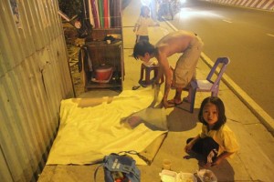 Buổi tối, anh Tuấn vẫn tiếp tục làm công việc dán điện thoại, laptop. Anh cho biết, ngày nào cao thì được hơn 100.000 đồng. Anh trải tấm bạt nhỏ làm nơi sinh hoạt cho hai đứa trẻ.